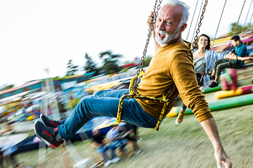 Happy mature man having fun on a chain swing ride at amusement park and looking at camera. Blurred motion.