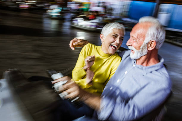 Cheerful mature couple in bumper car in blurred motion. Cheerful senior couple having fun in bumper car at amusement park. Blurred motion. couple driving at night stock pictures, royalty-free photos & images