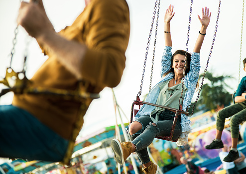 Young carefree woman having fun while riding on chain swing at amusement park and looking at camera.