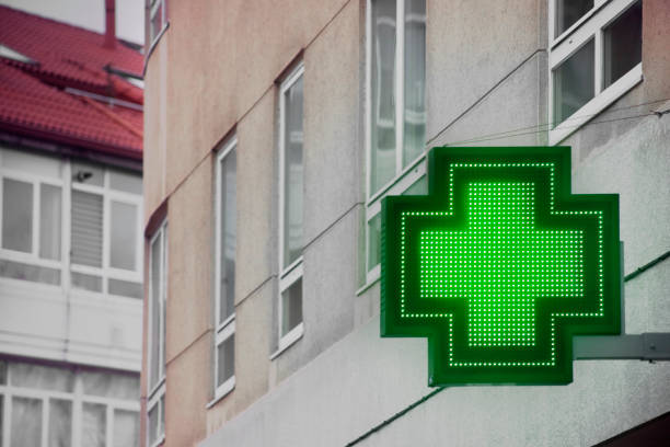 simbolo della farmacia in strada, edifici, croce verde. - green cross foto e immagini stock