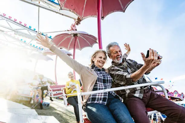 Photo of Happy senior couple taking a selfie during amusement park ride.
