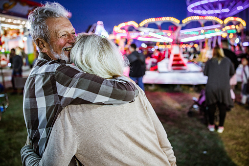 Happy affectionate seniors enjoying at amusement park by night/