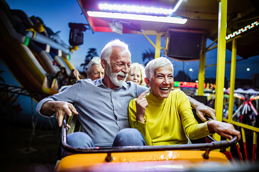Happy senior couple having fun while riding on rollercoaster in amusement park at night.