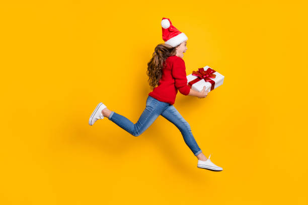 foto del profilo a grandezza naturale di una piccola signora pazza che salta in alto prendendo giftbox da babbo natale in x-mas midnight indossa pullover a maglia rossa e jeans sfondo giallo isolato - golf women surprise playing foto e immagini stock