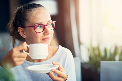 Happy teenage girl enjoying a cup of hot tea in the morning.\nNikon D850