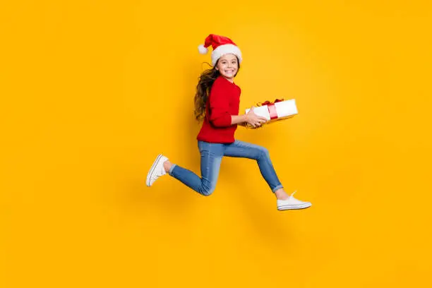 Full size profile photo of crazy little lady jumping high taking giftbox from santa, in x-mas midnight wear red knitted pullover and jeans isolated yellow background