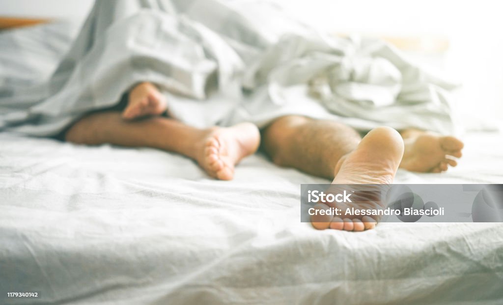 Close-up van mannelijke en vrouwelijke voeten op een bed-liefdevolle paar het hebben van seks onder onder witte deken in de slaapkamer-concept van sensuele en intieme moment van de liefhebbers-Vintage filter-focus op mannelijke voet - Royalty-free Bed Stockfoto