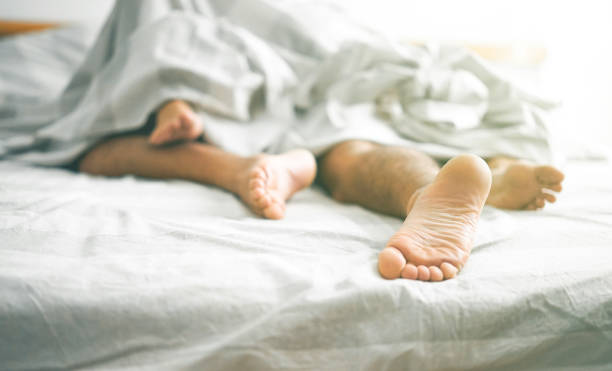 close up of male and female feet on a bed - loving couple having sex under under white blanket in the bedroom - concept of sensual and intimate moment of lovers - vintage filter - focus on male foot - infidelity sensuality couple men imagens e fotografias de stock