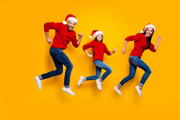 Photo of Full length body size of crazy smiling joyful happy family running for festive goods discounted wearing jeans denim red sweater santa cap headwear footwear speed fast excited isolated over vivid color background