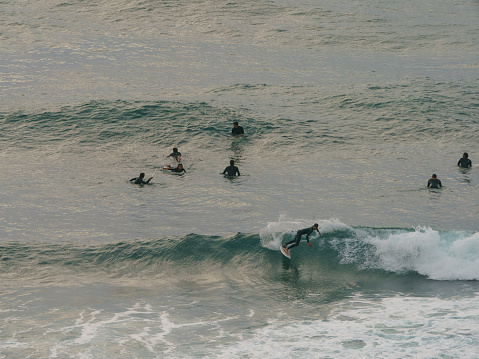 Bilbao, Spain - June 8, 2019: Water splashes around young surfers riding an epic barrel wave. Extreme pro sportsmen surfing a wave in summer sunny sunset.