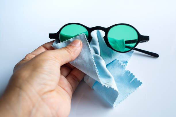 istock Woman's left hand cleaning black sunglasses by microfibre cleaning cloths, On white background, Close up & Macro shot, Selective focus, Optical concept 1179353442