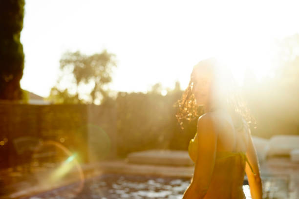 Beautiful young woman looking back during sunset. Millennial female is wearing bikini at back yard. She is enjoying weekend at poolside.