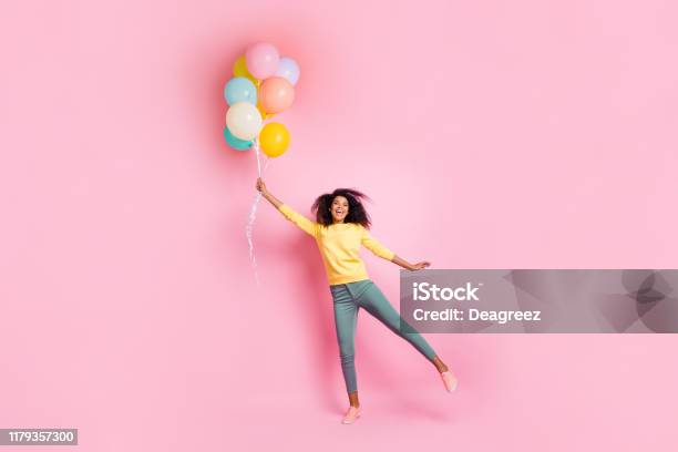 Full length photo of funky childish dreamy african girl hold many balons try fly in air enjoy holidays anniversary wear good look outfit sneakers isolated over pink color background