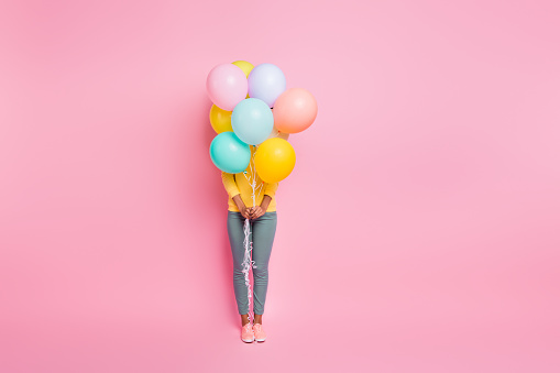Hide-and-seek concept. Full body photo of pretty cute nice happy ten girl having party on birthday, hiding behind many ballons hold in hands isolated pastel multicolored background