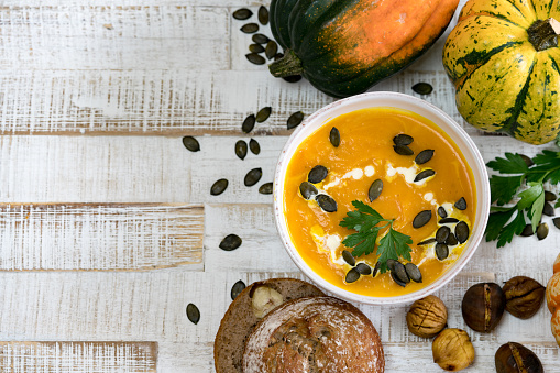 Delicious organic pumpkin soup in a white bowl framed by chestnuts pumpkins parsley and chestnut bread with copy space
