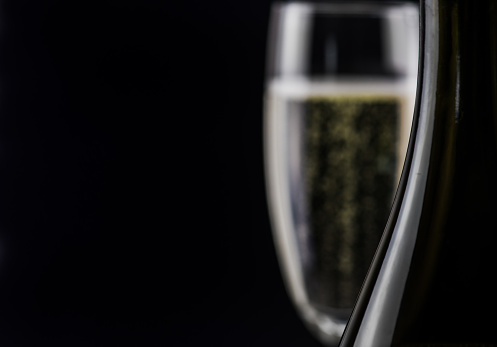 Champagne glass and bottle against black background with copy space