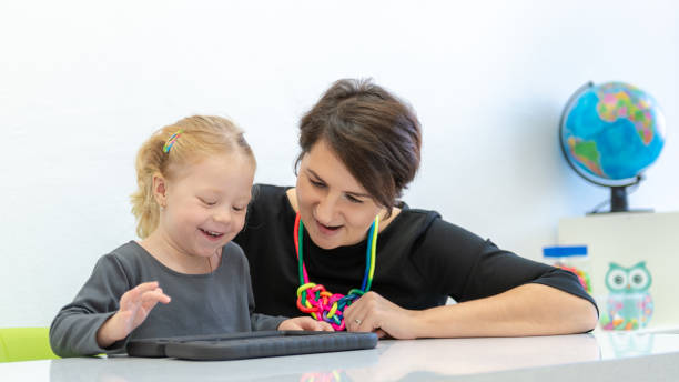 bambina in sessione di terapia occupazionale infantile che fa esercizi giocosi su un tablet digitale con il suo terapista. - physical and occupational therapists foto e immagini stock