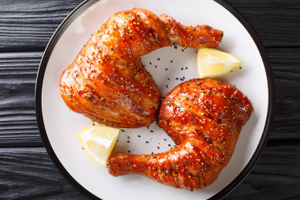 portion of sticky chicken quarter legs with sesame seeds and lemon close-up. Horizontal top view portion of sticky chicken quarter legs with sesame seeds and lemon close-up on a plate. Horizontal top view from above sticky sesame chicken sauces stock pictures, royalty-free photos & images