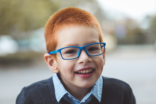 Front view of a boy wearing eyeglasses with his hands on his face looking at camera with amazing expression on blue background. Little amazed boy.