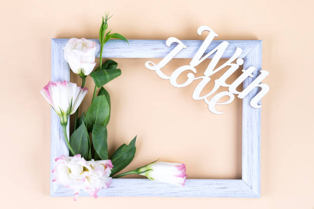 istock Empty white frame, With Love word and flowers eustoma on beige paper background with copy space. Holiday concept 1179385124