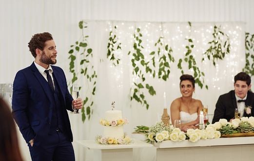 Shot of a young man giving a toast and speech at a wedding reception