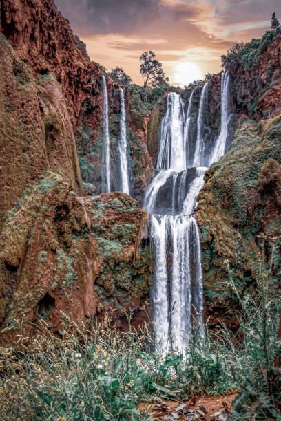 istock A bottom-up view of waterfall surrounded with green grass and orang colour terrain, 1179395913
