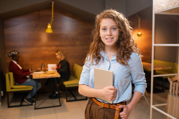 istock Pretty young smiling student with mobile gadget standing in front of camera 1179396060