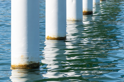 Rusty pier posts in salt sea water. White columns diagonal. Pillars mount for bridge. Sunny weather.