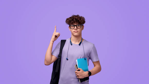 Amazed teen nerd pointing up Shocked youngster in nerdy glasses looking at camera and pointing up during studies at school against purple background nerd teenager stock pictures, royalty-free photos & images