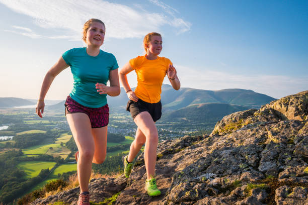 active young women trail running up mountain overlooking green valley - cumbria hiking keswick english lake district imagens e fotografias de stock