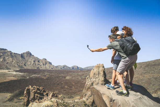 istock Mum, father and sons enjoying outdoors standing on a mountain cliff overlooking the panorama. Family making video story with action cam for the tourism blog. Holiday, travel, new trend tech concept. 1179408831