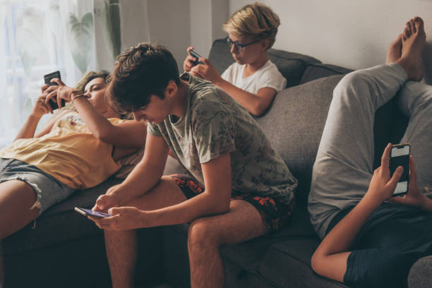 grupo de adolescentes que usan un teléfono inteligente sentado en un sofá en casa. los niños jóvenes y una chica compartiendo fotos y videos viendo historia social en línea. amigos disfrutando de la nueva tecnología de tendencias. concepto de juventu - malos hábitos fotografías e imágenes de stock