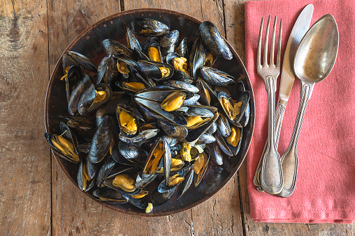 Plate with cooked mussels and cutlery top view on the wooden background