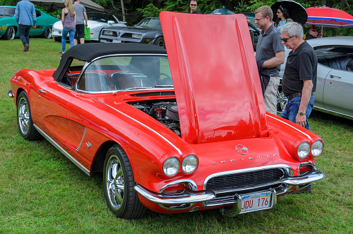 Moncton, New Brunswick, Canada - July 8, 2017 :  First generation Covette, 1962 Chevy Corvette with engine hood up, parked in Centennial Park during 2017 Atlantic Nationals Automotive Extravaganza. Two men stand near the classic Vette and give it a look over while other people walk among the classic cars on display.