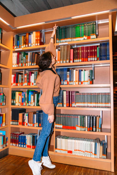 istock Young girl pulls book from top shelf of bookcase 1179418334