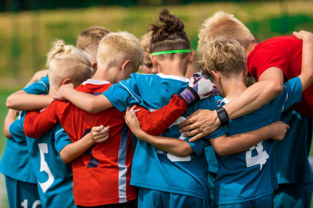 entrenador deportivo juvenil brujos niños en el campo de fútbol. niños acurrucados antes del partido final del torneo. niños agachados en el apiñado - competición de fútbol fotografías e imágenes de stock