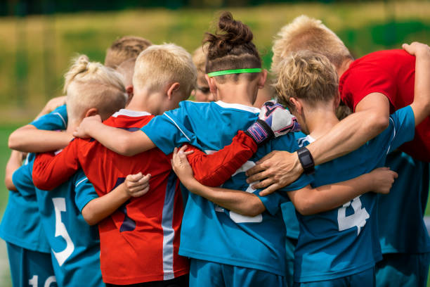 youth sports coach witch children on soccer field. kids huddling before the final tournament match. kids bending down in huddle - soccer ball youth soccer event soccer imagens e fotografias de stock