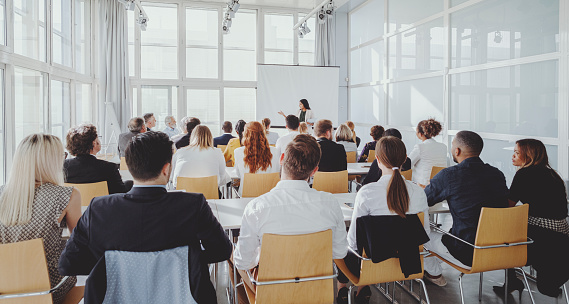 Businesswoman presenting SWOT analysis on large screen in spacious office room. Diverse audience viewed from back, clapping hands. Corporate setting.