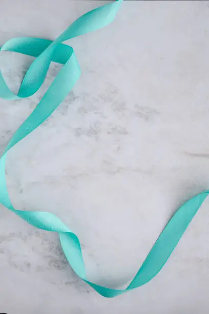 Light blue curled ribbon on white marble table, overhead. Copy space for text. Beauty blogging. ad layout.