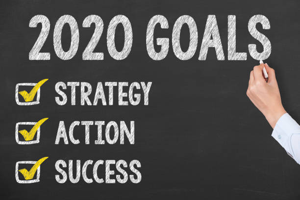 Human Hand Writing New Year 2020 Goals on Chalkboard Background