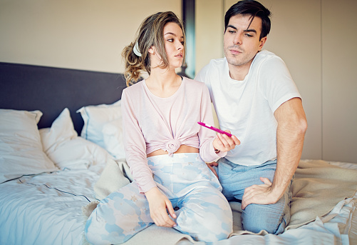 Shocked couple is looking positive pregnancy test in the bedroom