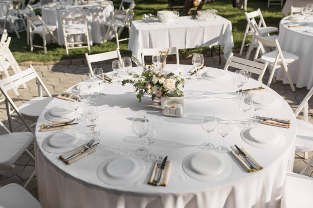 istock Wedding table setting decorated with fresh flowers in a brass vase. Wedding floristry. Banquet table for guests outdoors with a view of green nature. Bouquet with roses, eustoma and eucalyptus leaves 1179443094