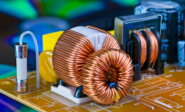 Toroidal inductor with copper wire winding, transformer and electric fuse. Detail of induction coil with magnetic ferrite core. Inverter. Current safeguard Close-up of electronic components on circuit board from dismantled power supply unit. Inductors on blue colored blurry background. Toroid coils. Electrotechnology electromagnetic photos stock pictures, royalty-free photos & images