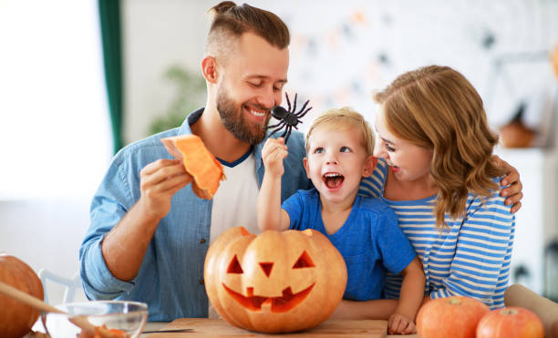 père heureux de mère de famille et fils d'enfant se préparent pour la maison de décorer d'halloween avec des citrouilles et riant, jouent et effrayer avec des araignées - spider mum photos et images de collection