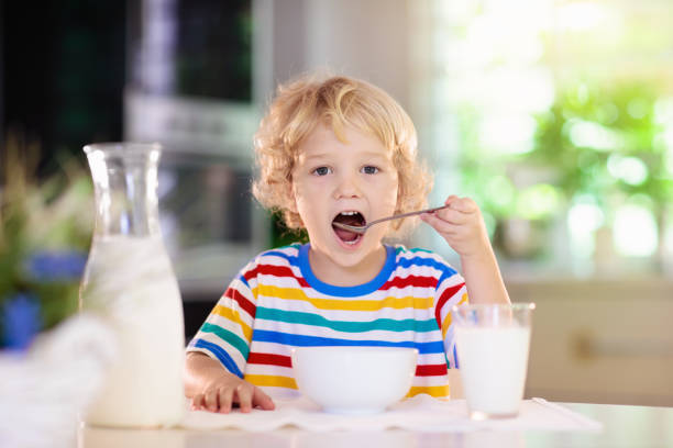Child eating breakfast. Kid with milk and cereal. Child having breakfast. Kid drinking milk and eating cereal with fruit. Little boy at white dining table in kitchen at window. Kids eat on sunny morning. Healthy balanced nutrition for young kids. boys bowl haircut stock pictures, royalty-free photos & images