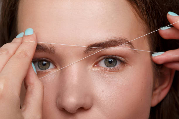 Eyebrow correction with a white thread Close-up of female face during eyebrow correction procedure hair threading stock pictures, royalty-free photos & images