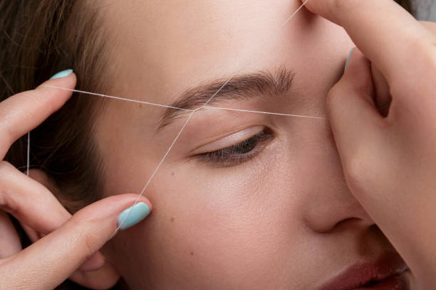 Eyebrow correction with a white thread Close-up of female face during eyebrow correction procedure hair threading stock pictures, royalty-free photos & images