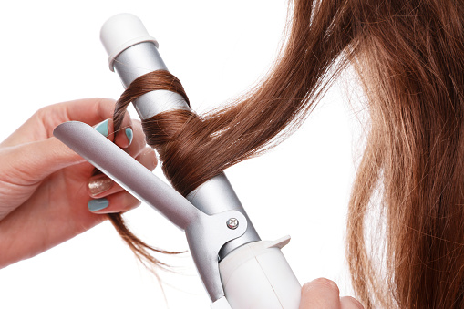 Curling iron and hair over white background