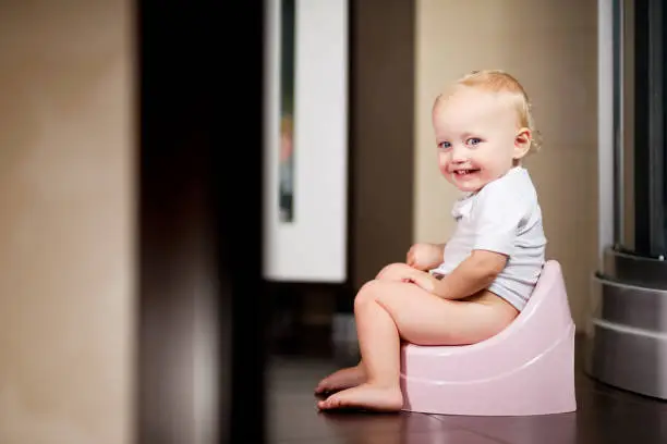 Baby girl sits on a pot in the bathroom and smiles