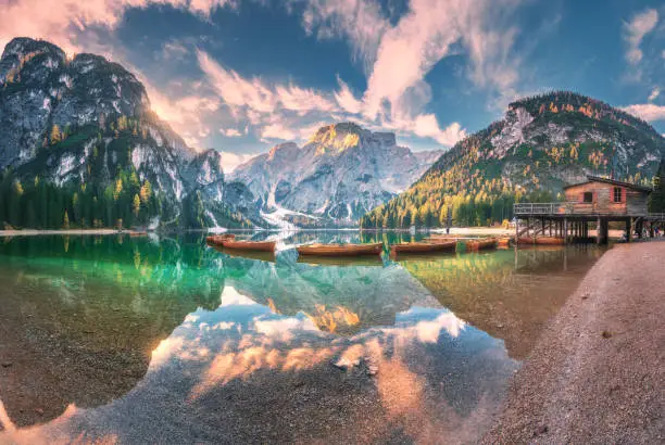 Amazing Braies lake at sunrise in autumn in Dolomites, Italy. Landscape with mountains, sky with clouds, boats, water with reflection, trees with colorful leaves. Lake in fall. Italian alps. Panorama